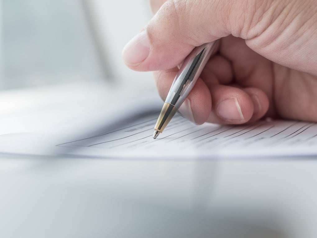 Eine Hand, die einen Stift über ein Blatt Papier hält Eine Hand, die einen Stift über ein Blatt Papier hält