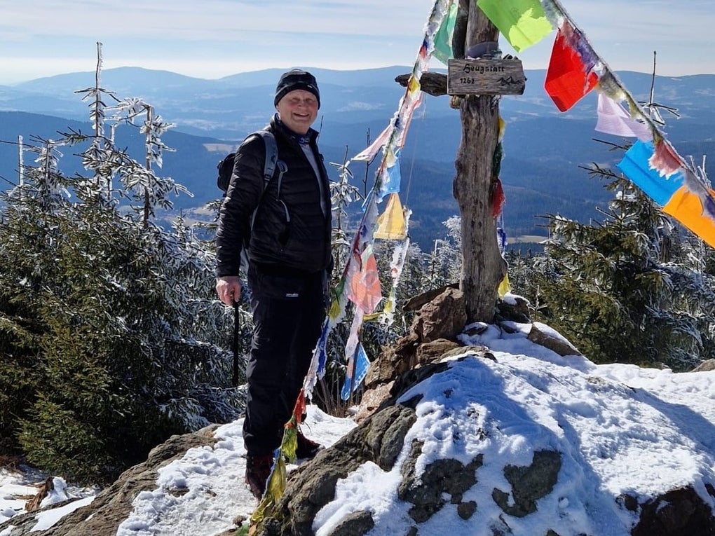 Martin steht neben einem Gipfelkreuz auf einem schneebedeckten Berg und lächelt in die Kamera. Martin steht neben einem Gipfelkreuz auf einem schneebedeckten Berg und lächelt in die Kamera.