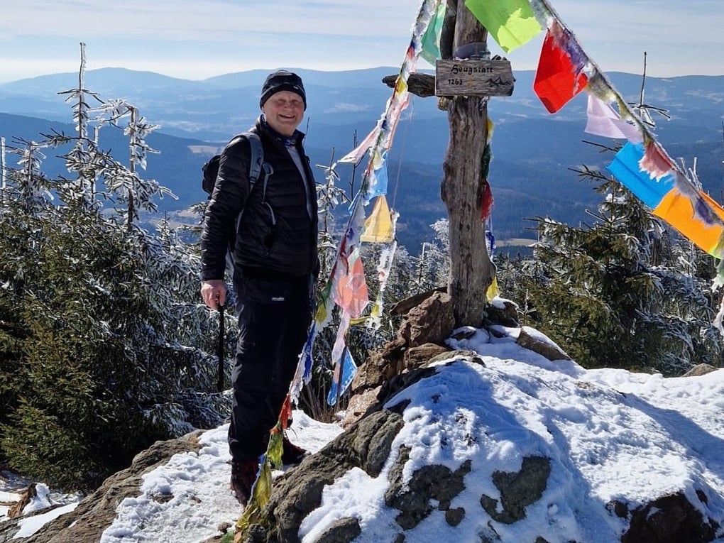 Martin steht neben einem Gipfelkreuz auf einem schneebedeckten Berg und lächelt in die Kamera. Martin steht neben einem Gipfelkreuz auf einem schneebedeckten Berg und lächelt in die Kamera.