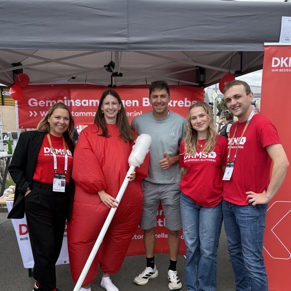 Eine Gruppe von Menschen, die an einem DKMS Stand für ein Foto posieren. Eine Gruppe von Menschen, die an einem DKMS Stand für ein Foto posieren.