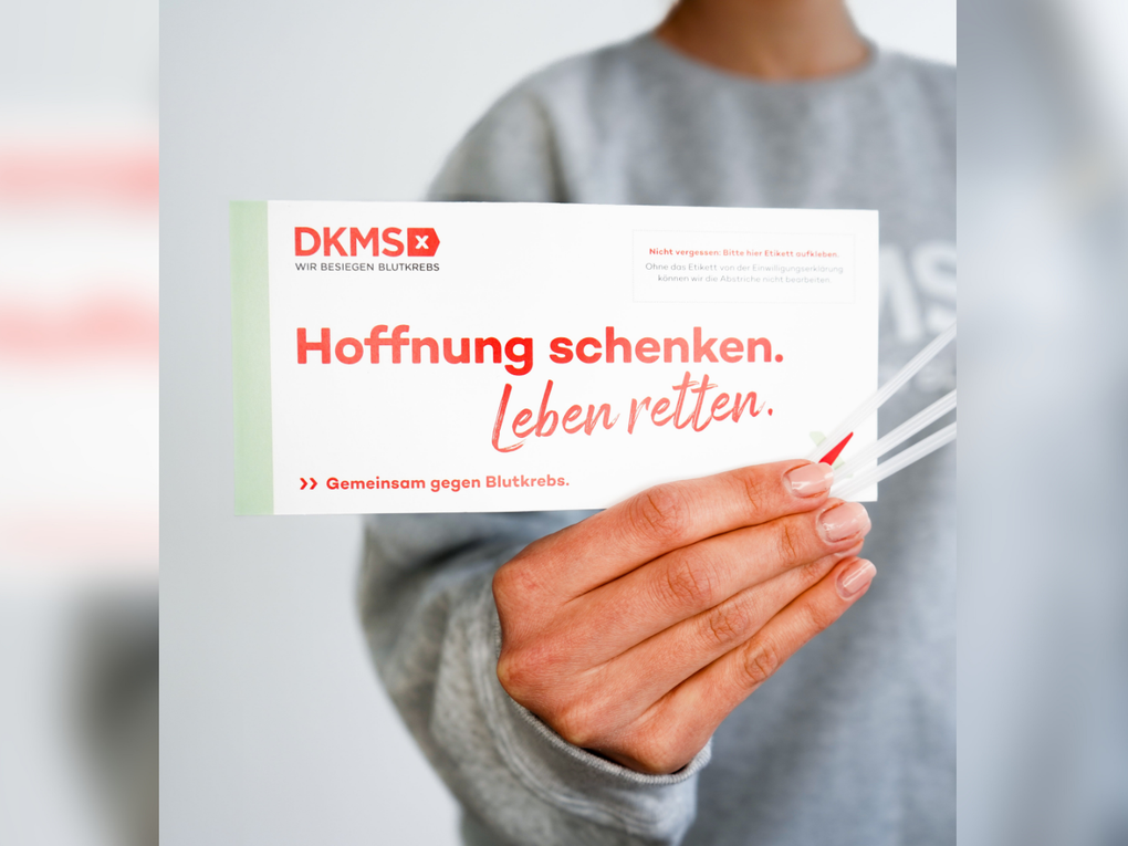 Eine Person trägt einen grauen Pullover und hält das DKMS Registrierungsset in die Kamera. Eine Person trägt einen grauen Pullover und hält das DKMS Registrierungsset in die Kamera.