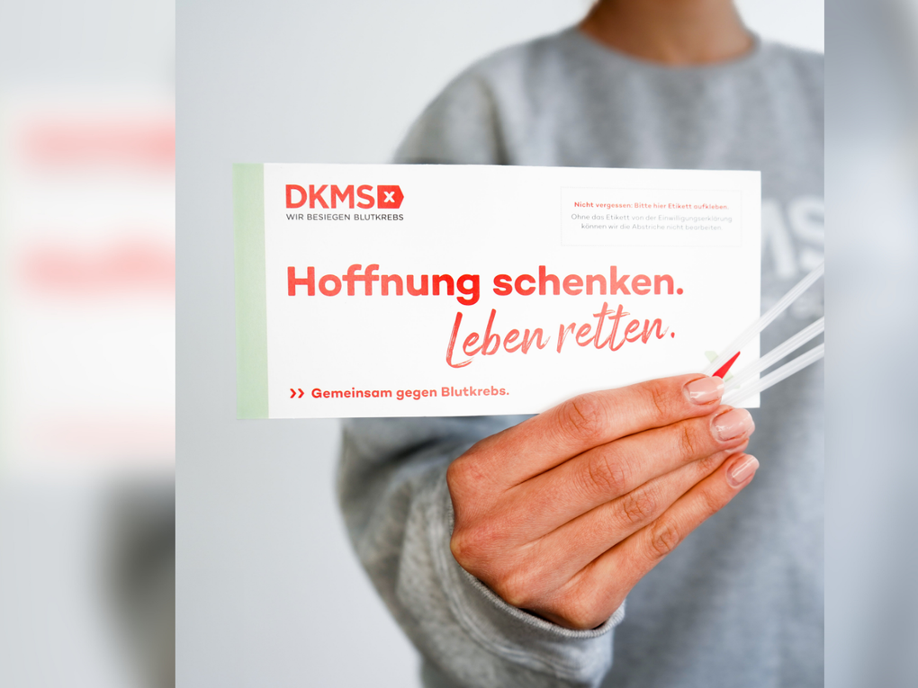 Eine Person trägt einen grauen Pullover und hält das DKMS Registrierungsset in die Kamera. Eine Person trägt einen grauen Pullover und hält das DKMS Registrierungsset in die Kamera.