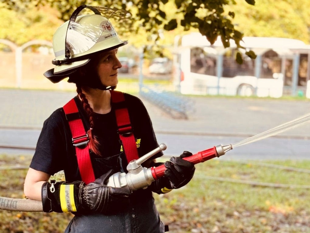 Eine Frau in Feuerwehrmontur hält einen Wasserschlauch in den Händen. Eine Frau in Feuerwehrmontur hält einen Wasserschlauch in den Händen.