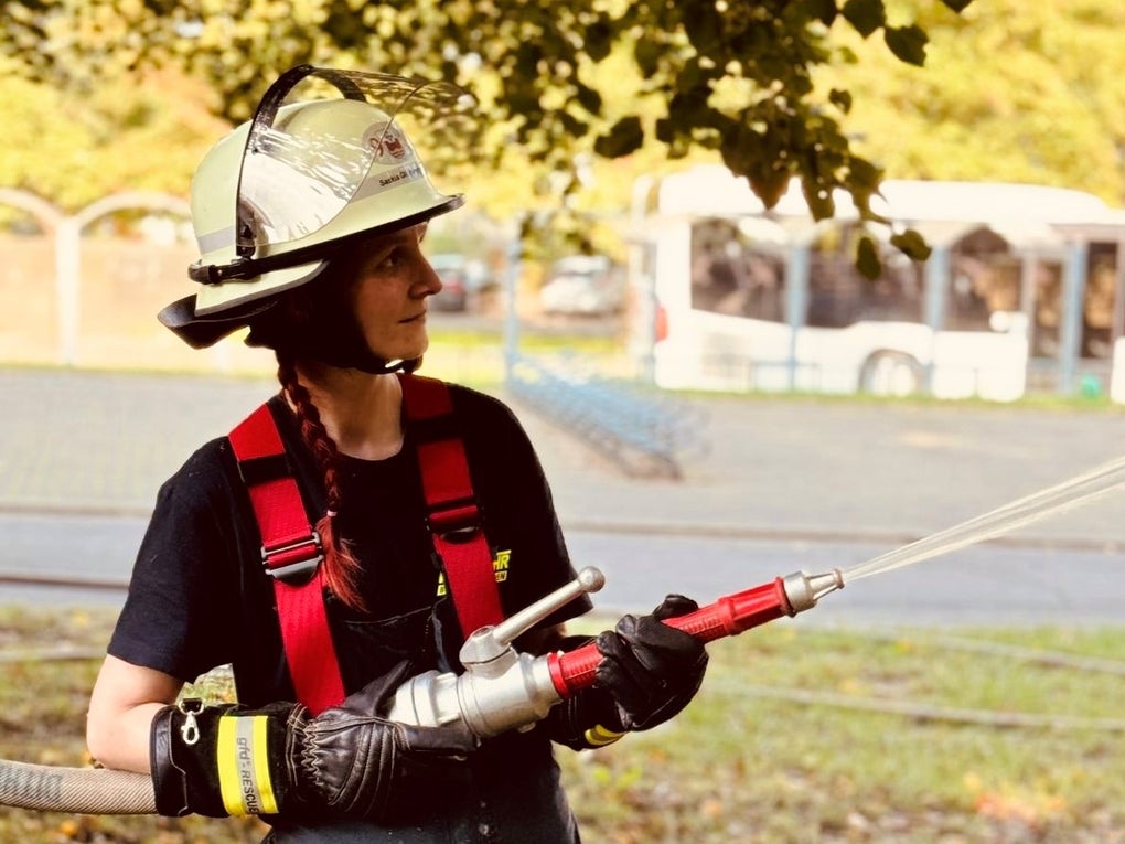 Eine Frau in Feuerwehrmontur hält einen Wasserschlauch in den Händen. Eine Frau in Feuerwehrmontur hält einen Wasserschlauch in den Händen.