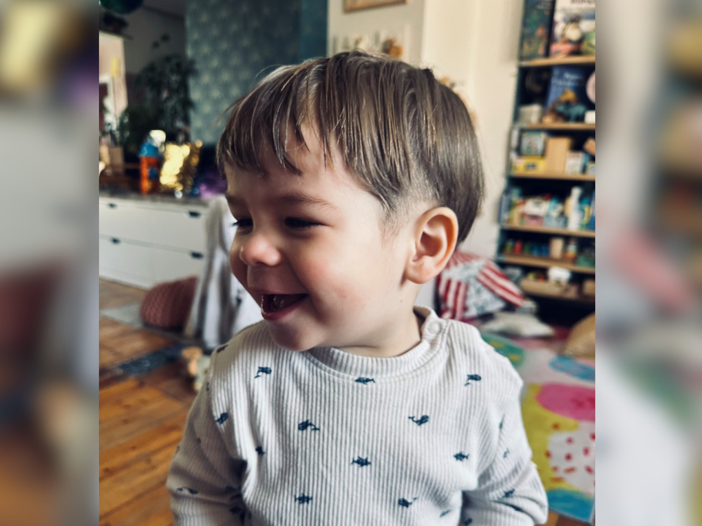 Ein kleiner Junge trägt einen grauen Pullover mit Wal-Aufdruck und lacht. Ein kleiner Junge trägt einen grauen Pullover mit Wal-Aufdruck und lacht.