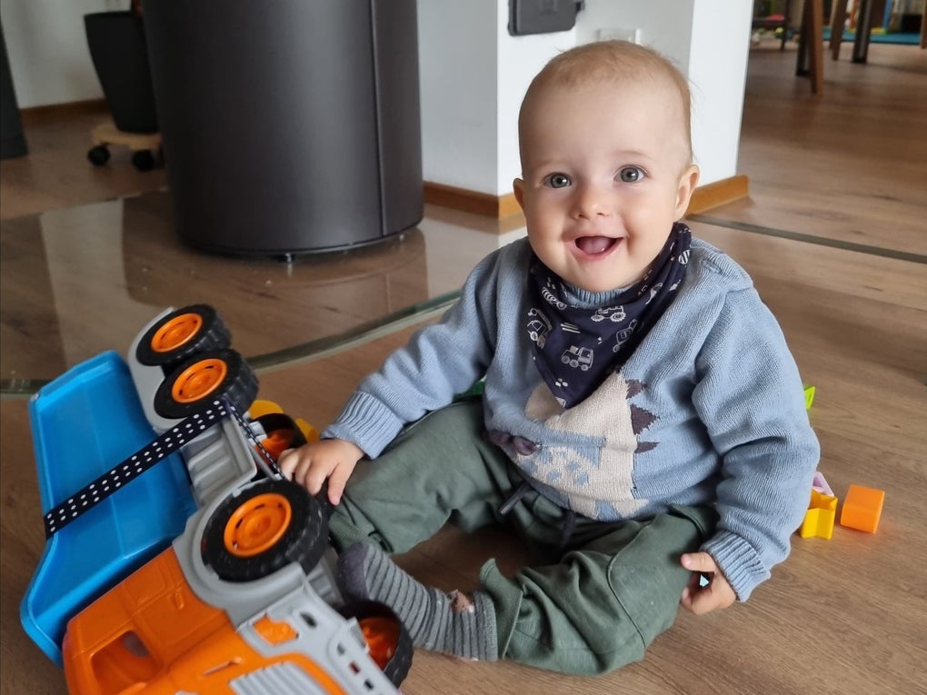 Ein Baby sitzt auf dem Boden und spielt mit einem Spielzeug-LKW Ein Baby sitzt auf dem Boden und spielt mit einem Spielzeug-LKW