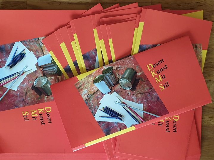 Ein Stapel roter Umschläge. Auf den Umschlägen ist ein Bild von Dosen und Malutensilien. Neben dem Bild steht "Dosen Kunst Mit Stil" Ein Stapel roter Umschläge. Auf den Umschlägen ist ein Bild von Dosen und Malutensilien. Neben dem Bild steht "Dosen Kunst Mit Stil"