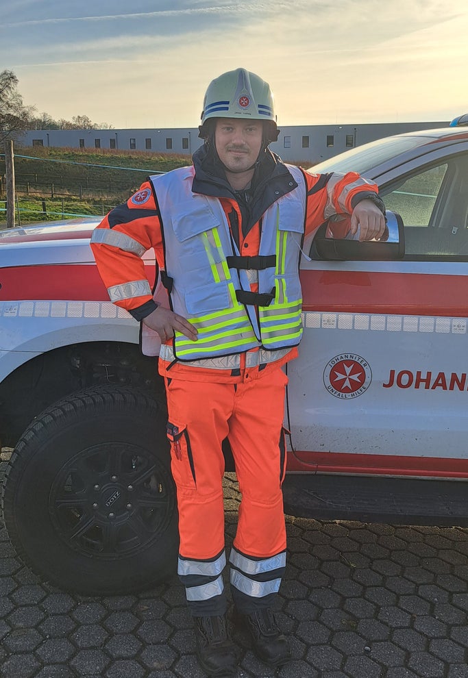 Jonas in Johanniter-Uniform vor einem Johanniter-Auto