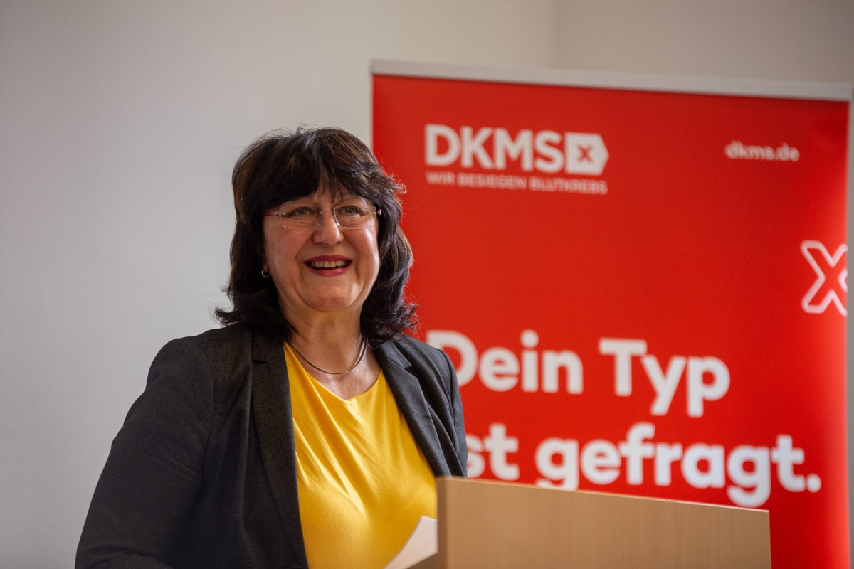 Frau mit dunklen Haaren, Brille und gelbem Oberteil steht an einem Rednerpult und lächelt. Im Hintergrund ist ein roter DKMS-Aufsteller mit der Aufschrift „Dein Typ ist gefragt“ zu sehen. Die Szene wirkt wie eine Veranstaltung oder ein Vortrag. Frau mit dunklen Haaren, Brille und gelbem Oberteil steht an einem Rednerpult und lächelt. Im Hintergrund ist ein roter DKMS-Aufsteller mit der Aufschrift „Dein Typ ist gefragt“ zu sehen. Die Szene wirkt wie eine Veranstaltung oder ein Vortrag.