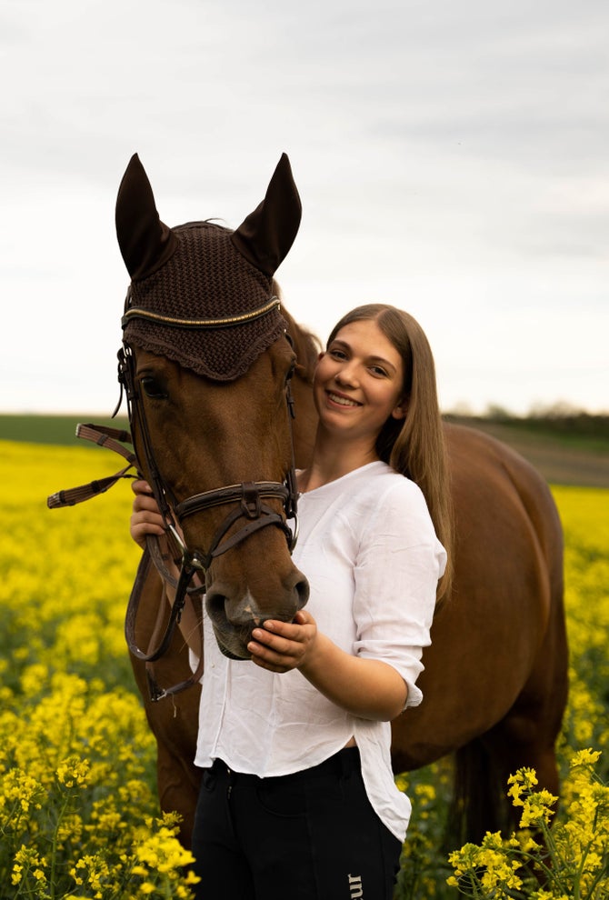 Patientin Franka steht lächelnd mit einem Pferd auf einer Wiese.