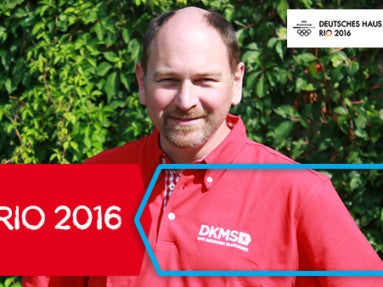 Ein Mann in einem roten Hemd mit DKMS Logo. Auf dem Bild ein rotes Banner mit der Aufschrift DKMS in Rio 2016 Ein Mann in einem roten Hemd mit DKMS Logo. Auf dem Bild ein rotes Banner mit der Aufschrift DKMS in Rio 2016