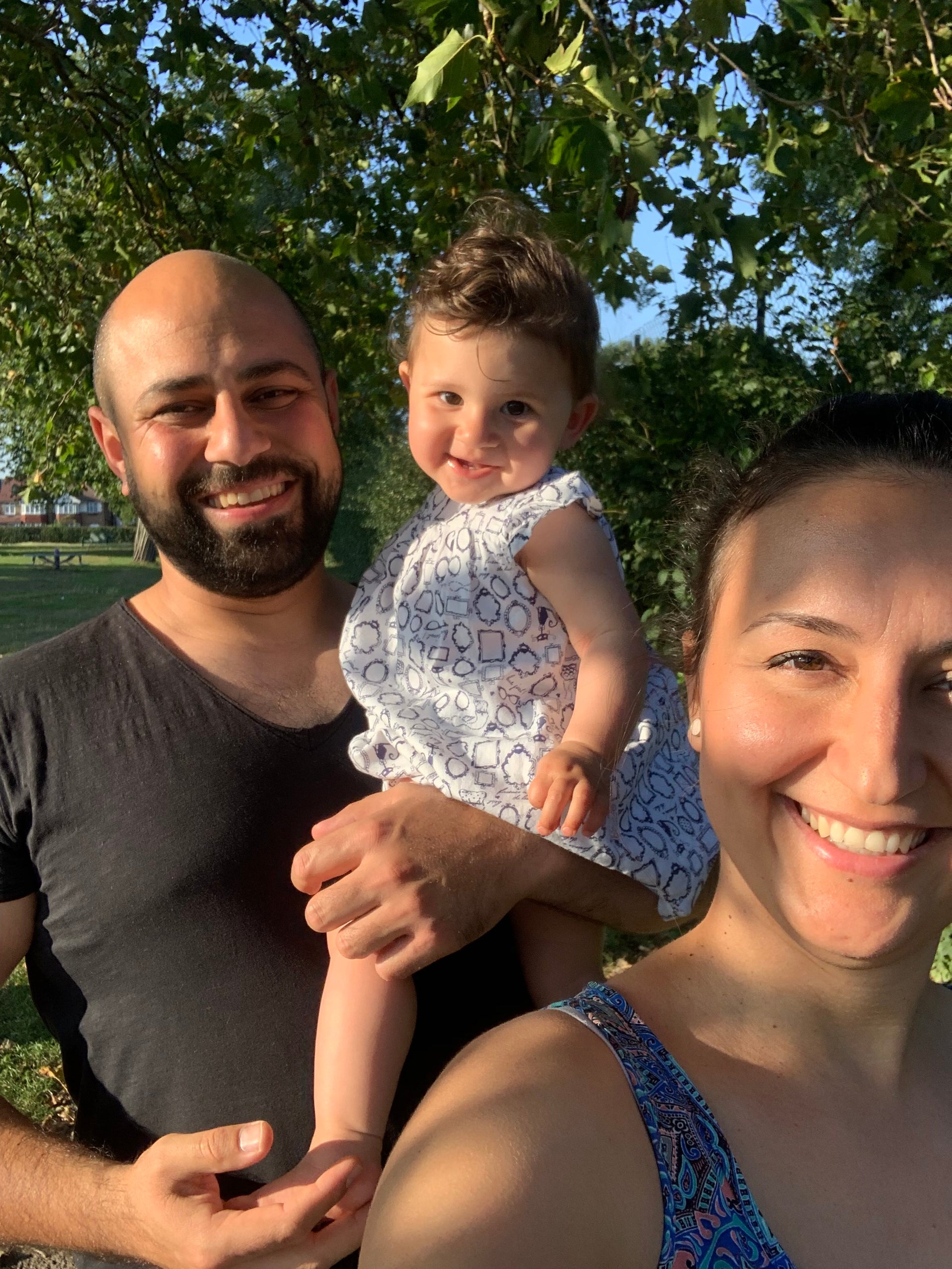 ein kleines Kind namens Liya mit ihrem Vater Ufuk und Mutter Hatice, das Mädchen ist bei ihrem Vater auf dem Arm, im Hintergrund sieht man einen Baum ein kleines Kind namens Liya mit ihrem Vater Ufuk und Mutter Hatice, das Mädchen ist bei ihrem Vater auf dem Arm, im Hintergrund sieht man einen Baum