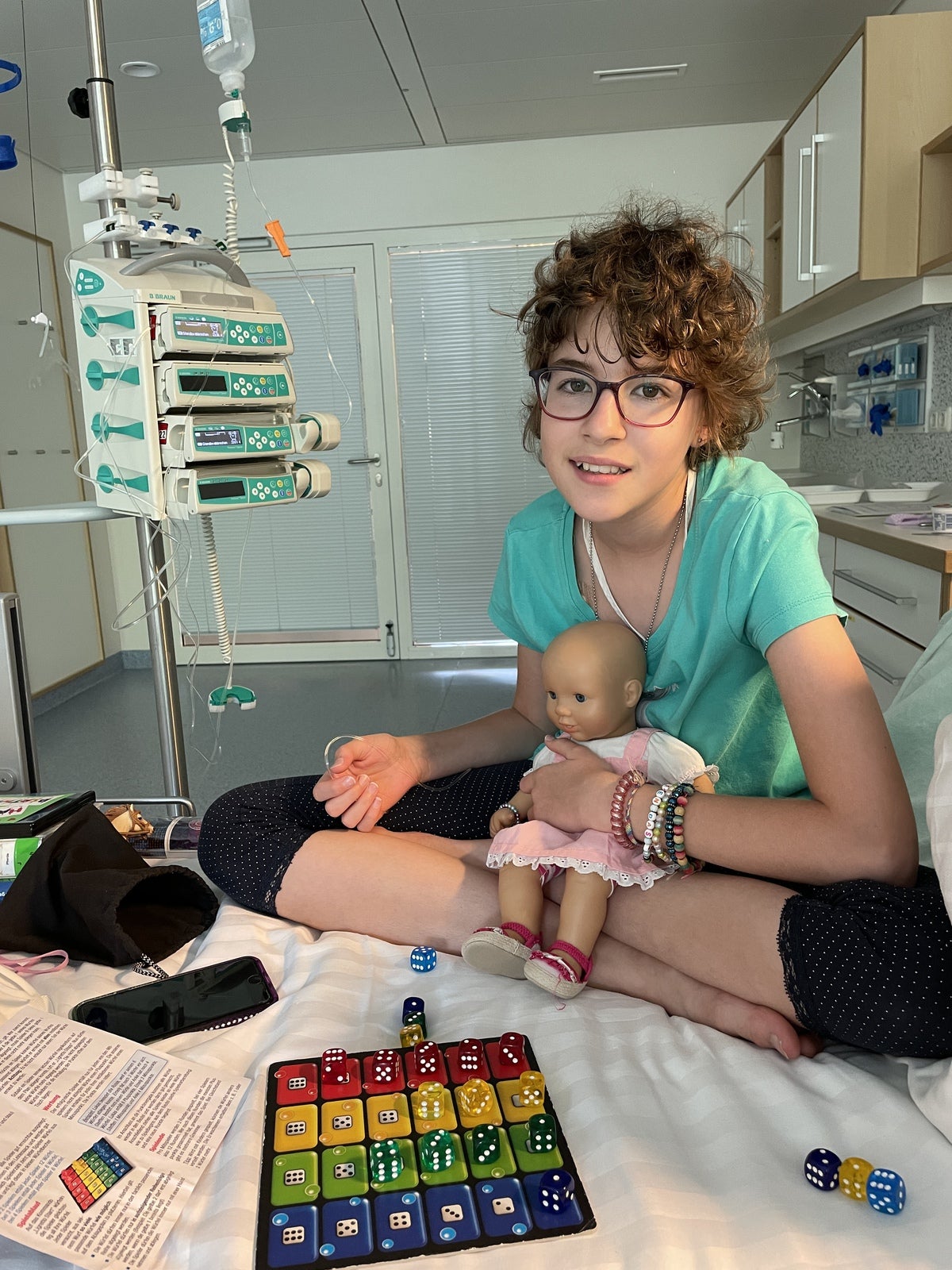 ein Mädchen sitzt mit einer Puppe und einem Spiel auf einem Krankenhausbett ein Mädchen sitzt mit einer Puppe und einem Spiel auf einem Krankenhausbett