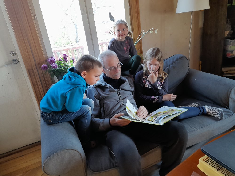 Frank sitzt auf dem Sofa und liest seinen Enkelkindern aus einem Buch vor.