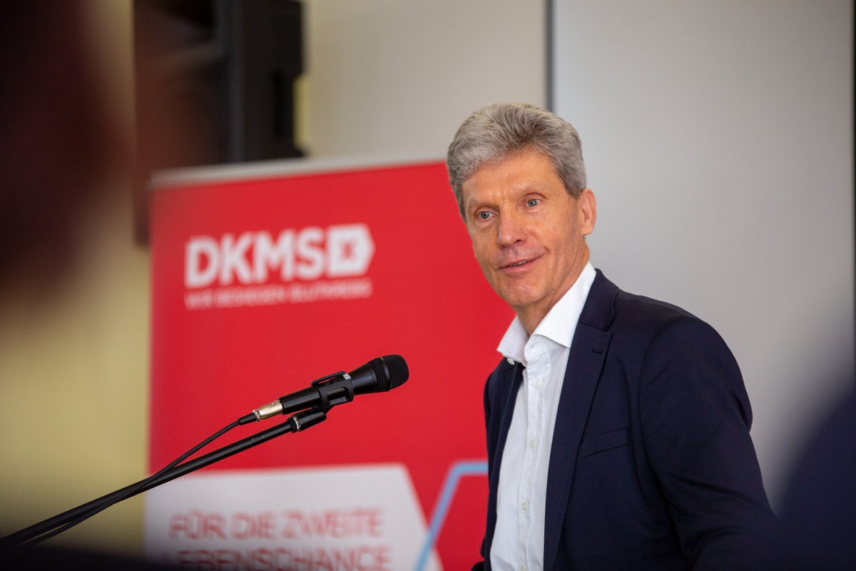 Mann mit grauen Haaren im dunklen Sakko spricht an einem Mikrofon. Im Hintergrund steht ein roter DKMS-Aufsteller mit dem Schriftzug „DKMS – Wir besiegen Blutkrebs“ und „Für die zweite Chance“. Mann mit grauen Haaren im dunklen Sakko spricht an einem Mikrofon. Im Hintergrund steht ein roter DKMS-Aufsteller mit dem Schriftzug „DKMS – Wir besiegen Blutkrebs“ und „Für die zweite Chance“.