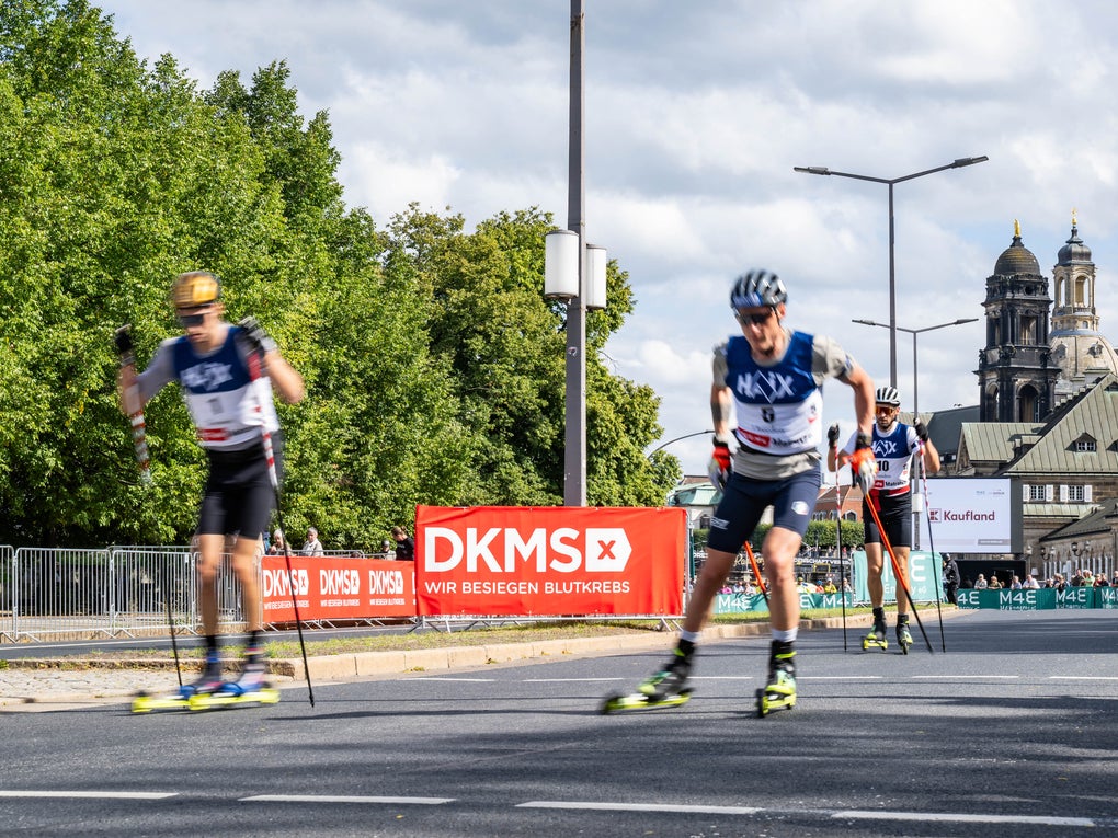 Biathlon-Athleten auf rollenden Skiern vor einem DKMS Banner und der Dresdner Skyline. Biathlon-Athleten auf rollenden Skiern vor einem DKMS Banner und der Dresdner Skyline.