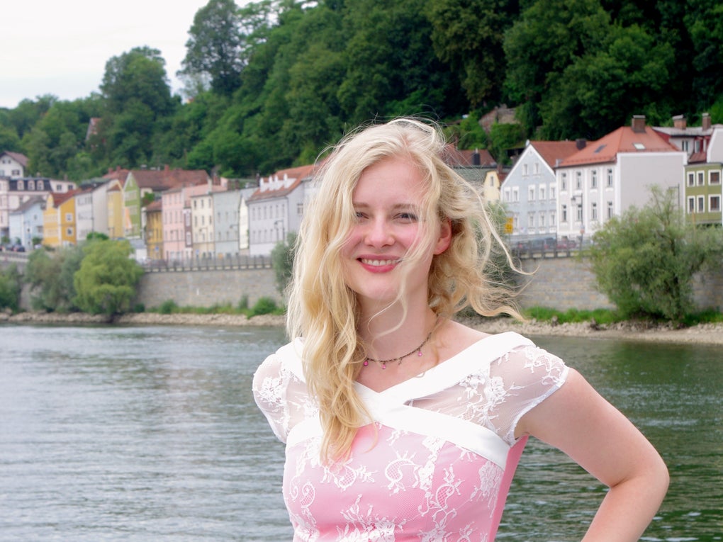 Eine Frau in einem rosa Kleid lehnt an einem Geländer auf einem Schiff, im Hintergrund ist Wasser Eine Frau in einem rosa Kleid lehnt an einem Geländer auf einem Schiff, im Hintergrund ist Wasser