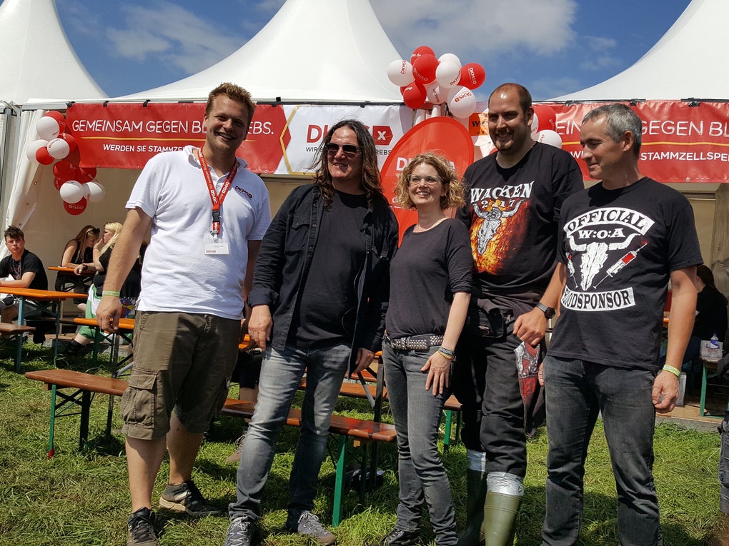 Eine Gruppe von Menschen steht auf Wacken vor einem Zelt der DKMS Eine Gruppe von Menschen steht auf Wacken vor einem Zelt der DKMS