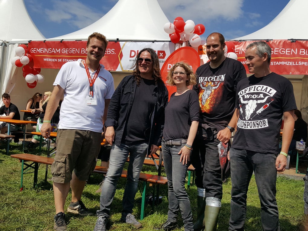 Eine Gruppe von Menschen steht auf Wacken vor einem Zelt der DKMS Eine Gruppe von Menschen steht auf Wacken vor einem Zelt der DKMS
