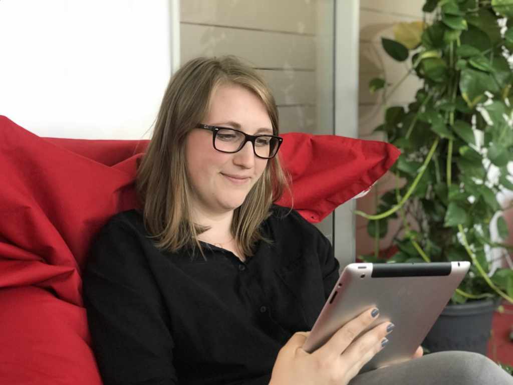 Sara von Knobelsdorff sitzt auf einem roten Kissen und hält ein Tablet Sara von Knobelsdorff sitzt auf einem roten Kissen und hält ein Tablet