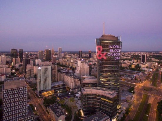 Eine Stadtsilhouette mit einem hohen Gebäude, auf dem mit Licht World Blood Cancer Day projiziert ist Eine Stadtsilhouette mit einem hohen Gebäude, auf dem mit Licht World Blood Cancer Day projiziert ist