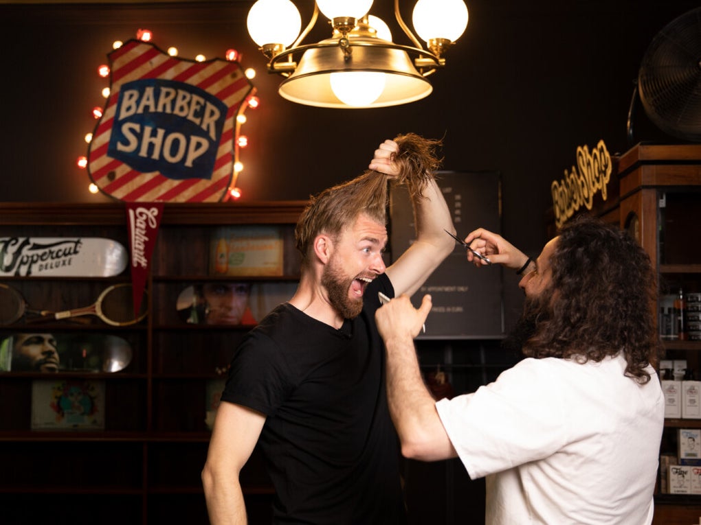 Daniel Korte hält seine langen Haare in einem Zopf hoch. Ein zweiter Mann hält eine Schere vor ihm. Daniel Korte hält seine langen Haare in einem Zopf hoch. Ein zweiter Mann hält eine Schere vor ihm.