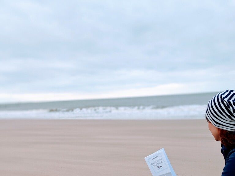 Eine Frau hält ein Buch an einem Strand Eine Frau hält ein Buch an einem Strand