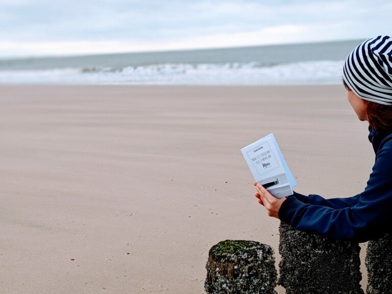 Eine Frau hält ein Buch an einem Strand Eine Frau hält ein Buch an einem Strand