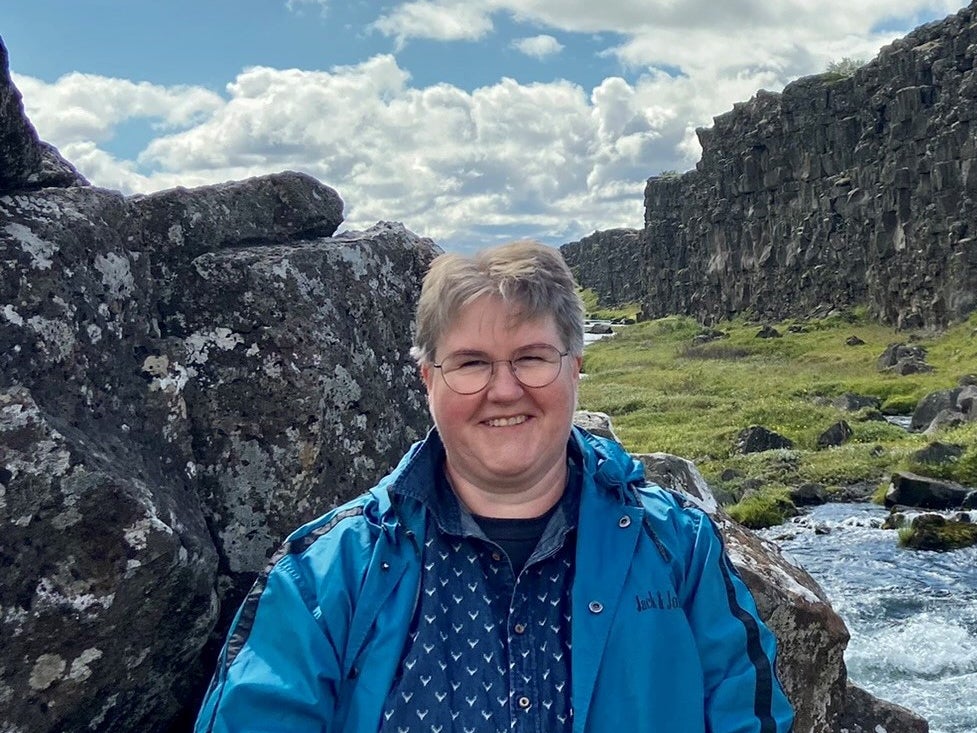 eine Frau sitzt auf einem Stein, im Hintergrund sieht man einen Fluss und Berge eine Frau sitzt auf einem Stein, im Hintergrund sieht man einen Fluss und Berge