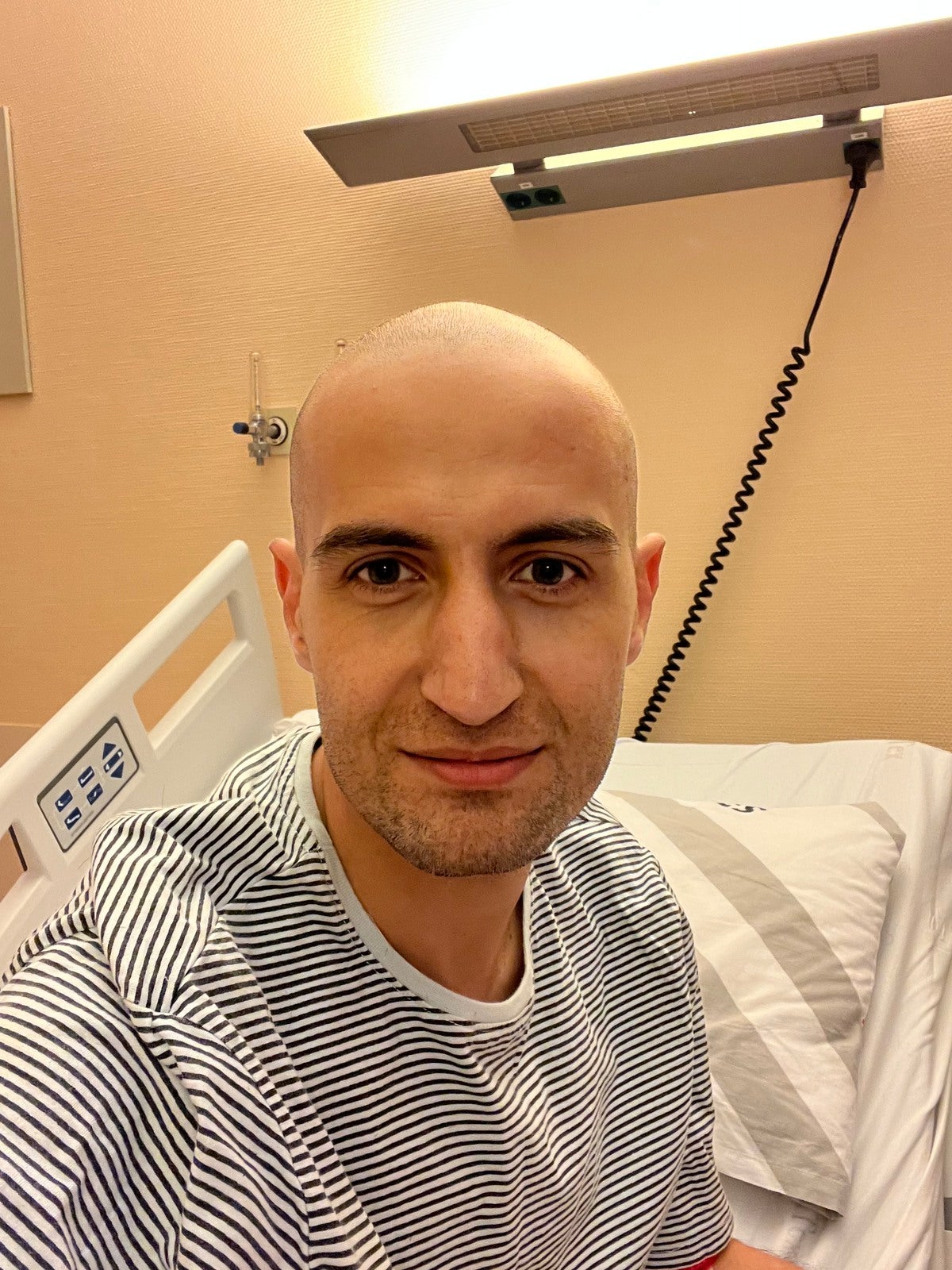 Mann mit Glatze lächelt für ein Selfie in einem Krankenhausbett Mann mit Glatze lächelt für ein Selfie in einem Krankenhausbett