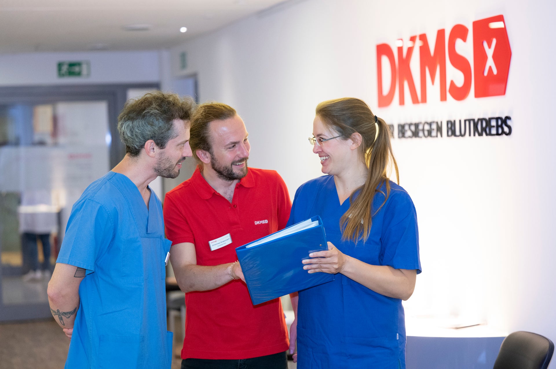 Eine Gruppe von Menschen in Kitteln, im Hintergrund das DKMS Logo Eine Gruppe von Menschen in Kitteln, im Hintergrund das DKMS Logo