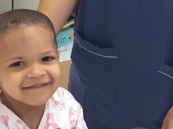 Ein Kind lächelt in die Kamera, rechts daneben steht eine Person in einem Kasack Ein Kind lächelt in die Kamera, rechts daneben steht eine Person in einem Kasack