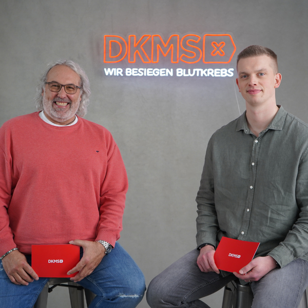 Zwei Männer sitzen auf Hockern und halten rote Aktenordner Zwei Männer sitzen auf Hockern und halten rote Aktenordner