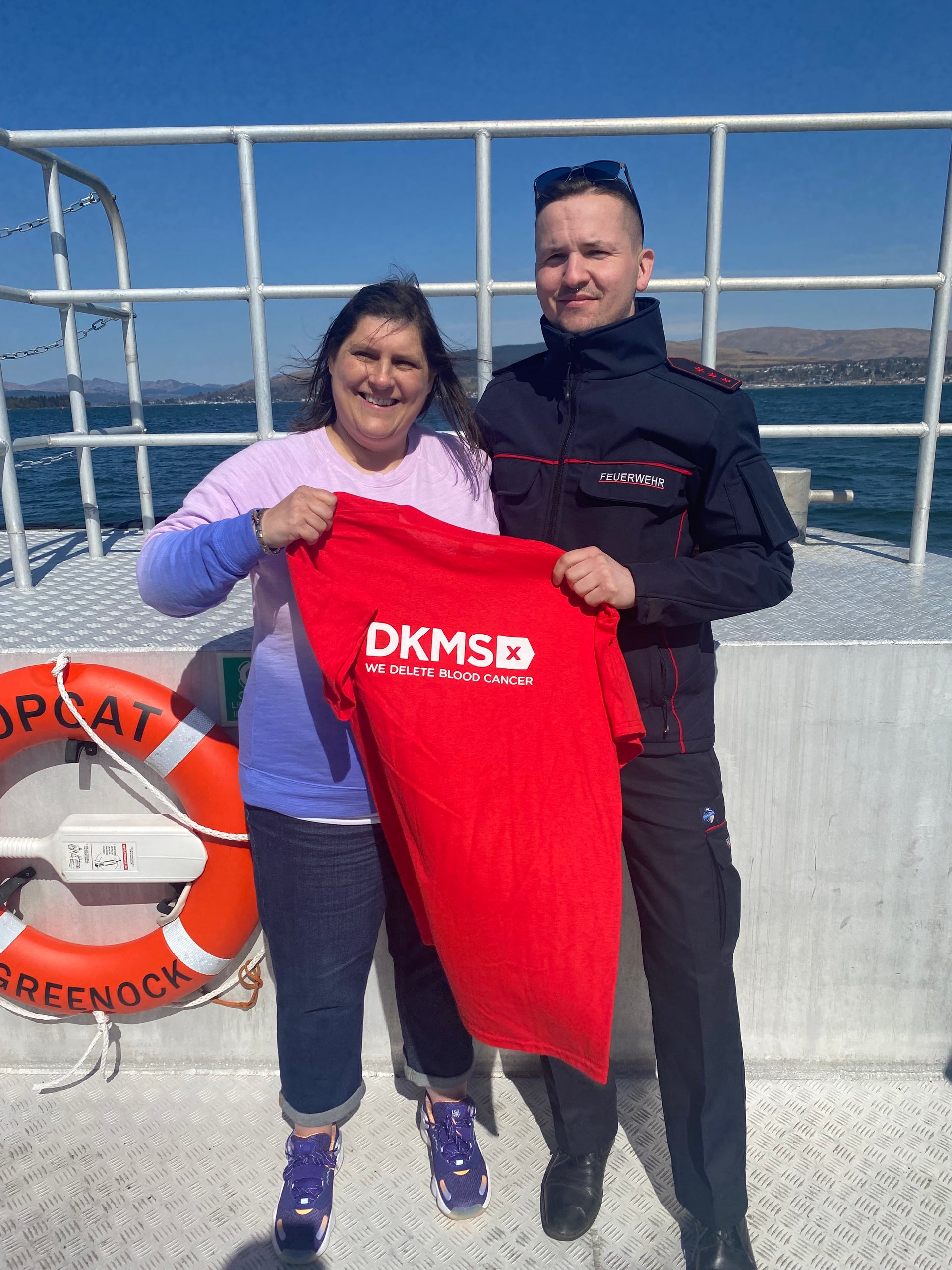 ein Mann und eine Frau stehen auf einem Boot und halten ein rotes DKMS T-Shirt zwischen sich hoch ein Mann und eine Frau stehen auf einem Boot und halten ein rotes DKMS T-Shirt zwischen sich hoch