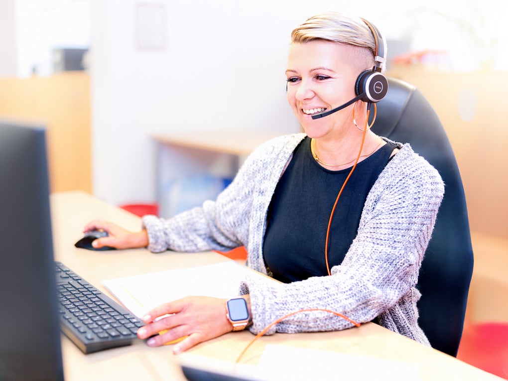 Eine blonde Frau, die ein Headset trägt und an einem Schreibtisch sitzt und telefoniert Eine blonde Frau, die ein Headset trägt und an einem Schreibtisch sitzt und telefoniert