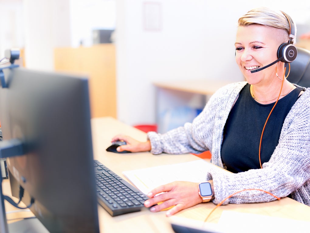 Eine blonde Frau, die ein Headset trägt und an einem Schreibtisch sitzt und telefoniert Eine blonde Frau, die ein Headset trägt und an einem Schreibtisch sitzt und telefoniert