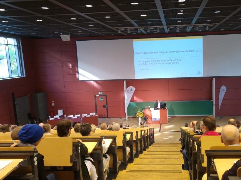 Eine Gruppe von Personen, die in einem Hörsaal mit einer Projektionsfläche sitzen Eine Gruppe von Personen, die in einem Hörsaal mit einer Projektionsfläche sitzen
