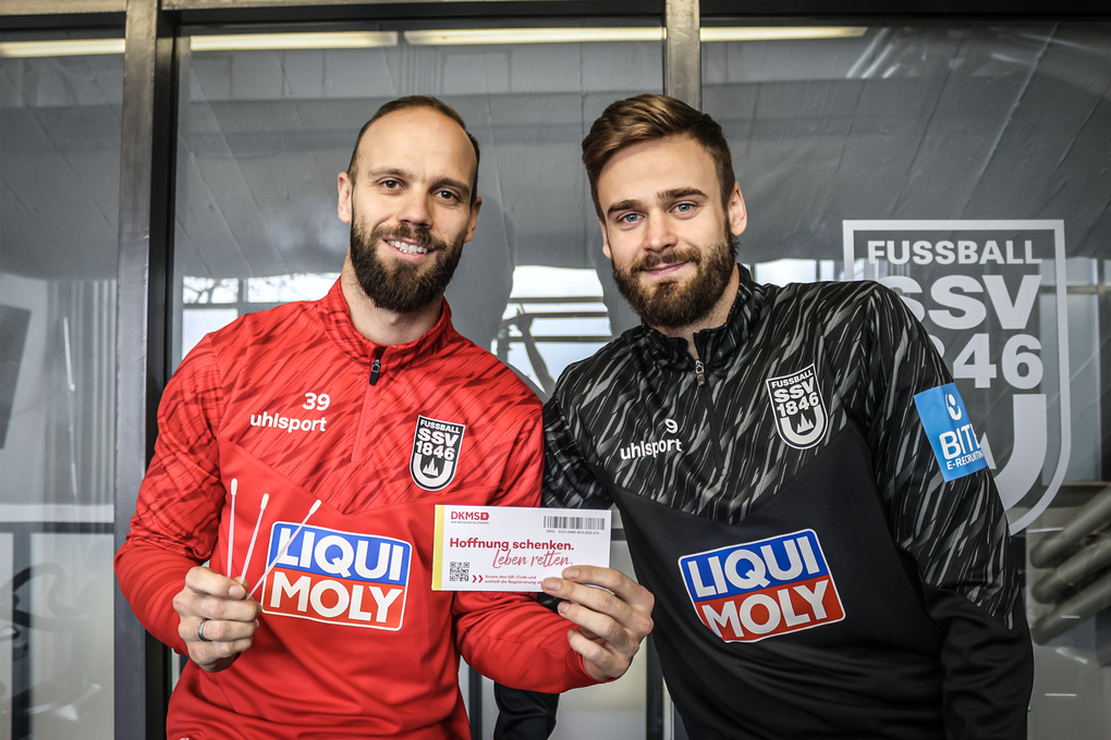 Zwei Männer halten ein DKMS Registrierungs-Kit Zwei Männer halten ein DKMS Registrierungs-Kit