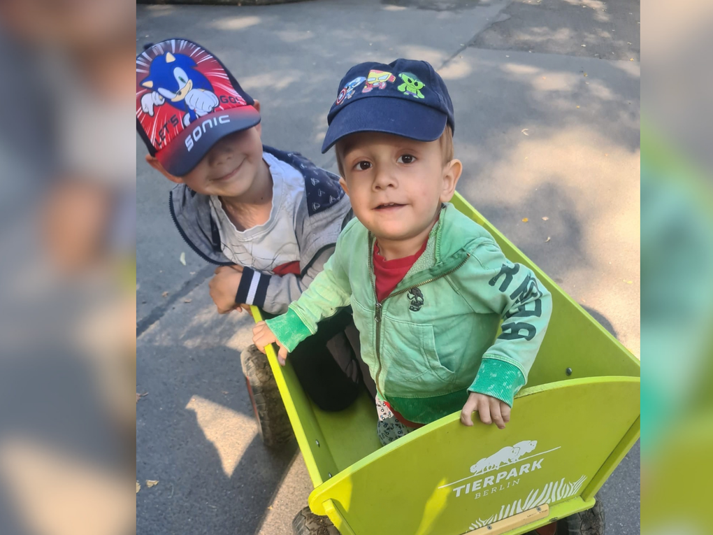 Zwei kleine Jungen tragen Kappen und sitzen in einem grünen Bollerwagen. Zwei kleine Jungen tragen Kappen und sitzen in einem grünen Bollerwagen.