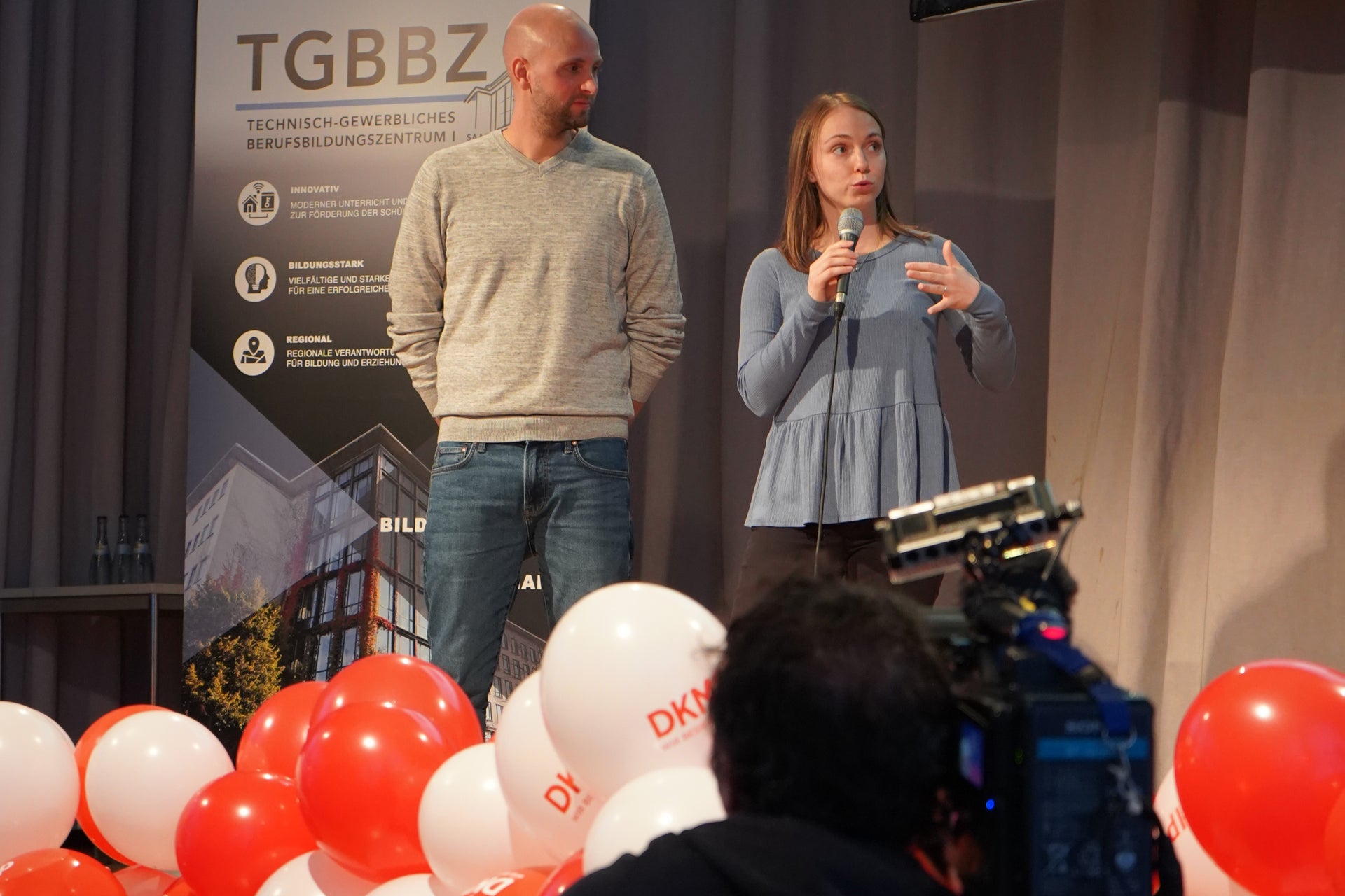 eine Frau und ein Mann stehen nebeneinandner auf einer Bühne eine Frau und ein Mann stehen nebeneinandner auf einer Bühne