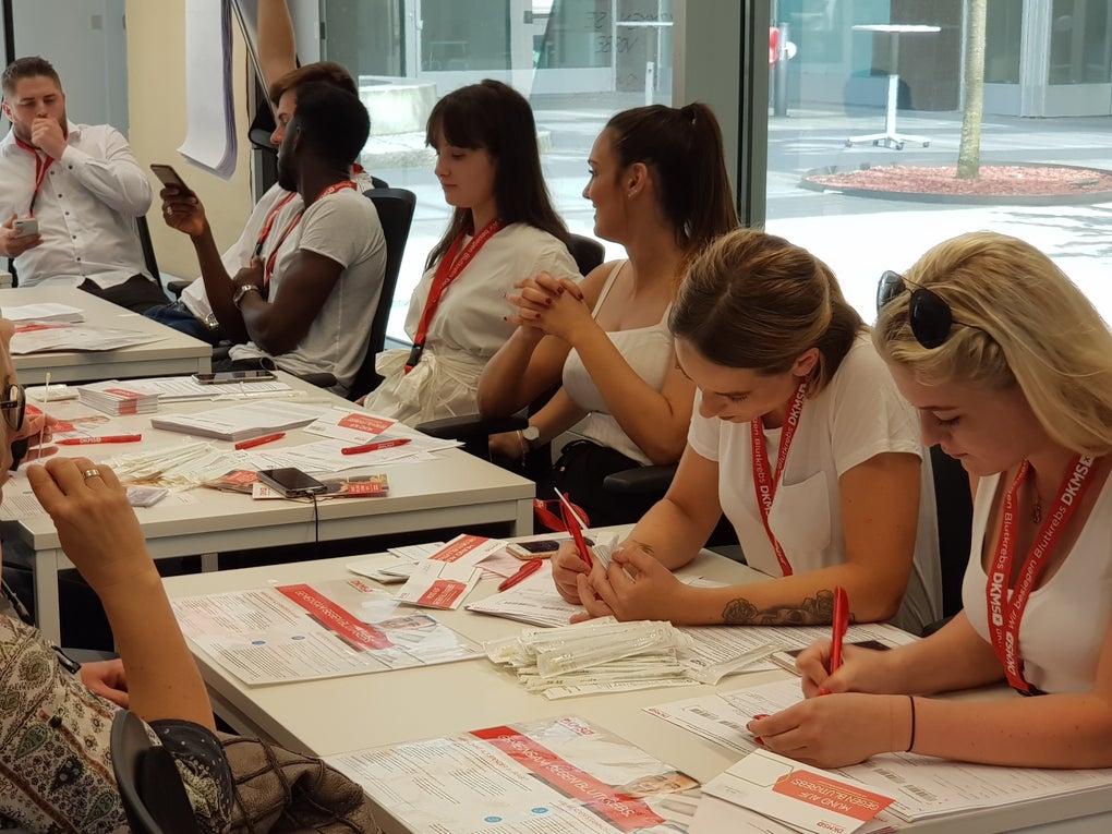 Eine Gruppe von Menschen, die sich gegenüber an Tischen sitzen Eine Gruppe von Menschen, die sich gegenüber an Tischen sitzen