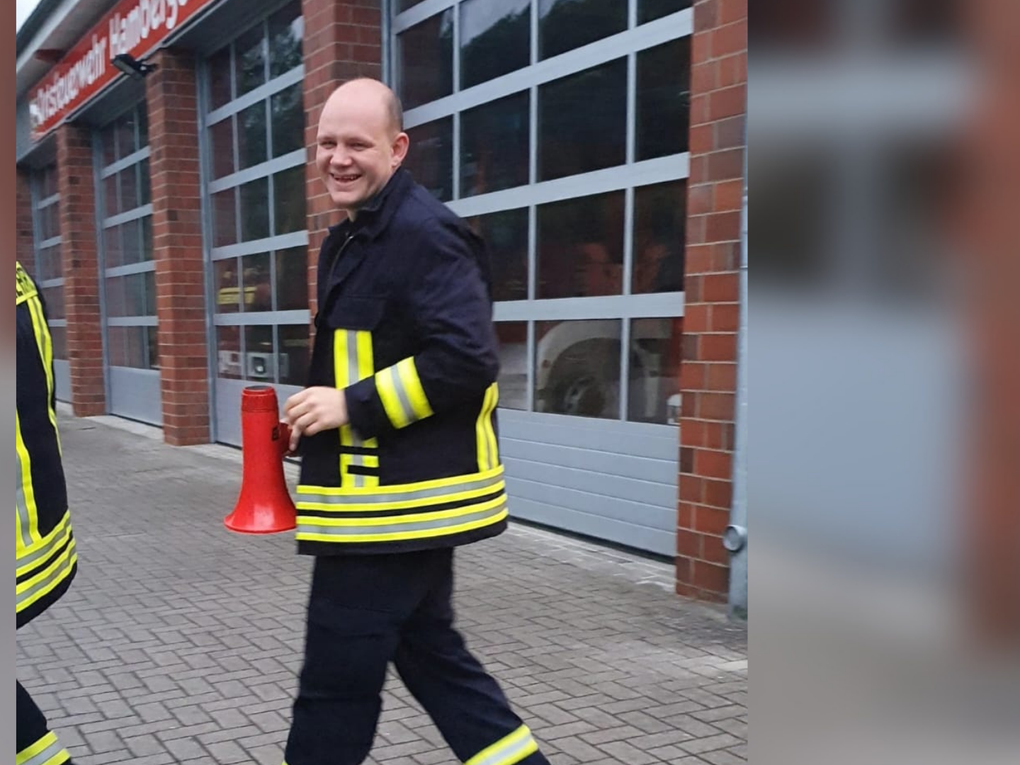 Ein Mann trägt eine Feuerwehruniform und hält ein rotes Megafon. Ein Mann trägt eine Feuerwehruniform und hält ein rotes Megafon.