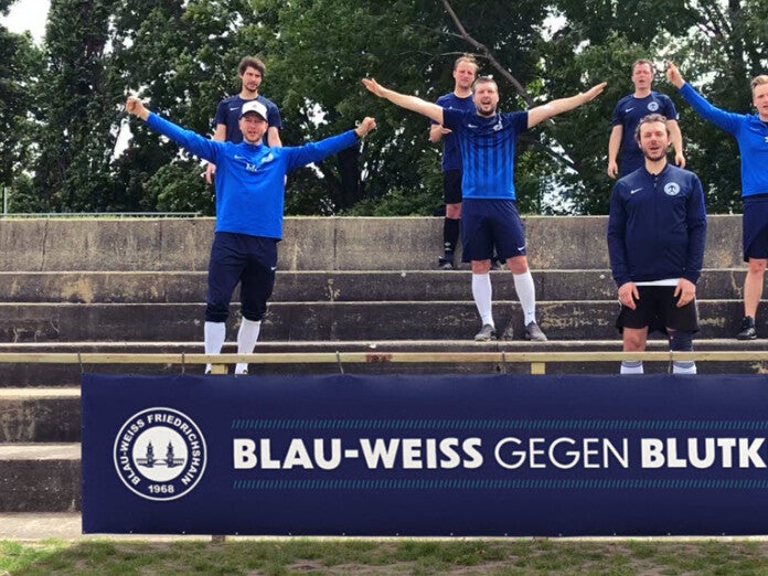 Eine Gruppe von Männern in blauen Uniformen steht mit erhobenen Armen auf einer Treppe. Darunter ist ein Banner mit dem Text "Blau-Weiss Gegen Blutkrebs" Eine Gruppe von Männern in blauen Uniformen steht mit erhobenen Armen auf einer Treppe. Darunter ist ein Banner mit dem Text "Blau-Weiss Gegen Blutkrebs"