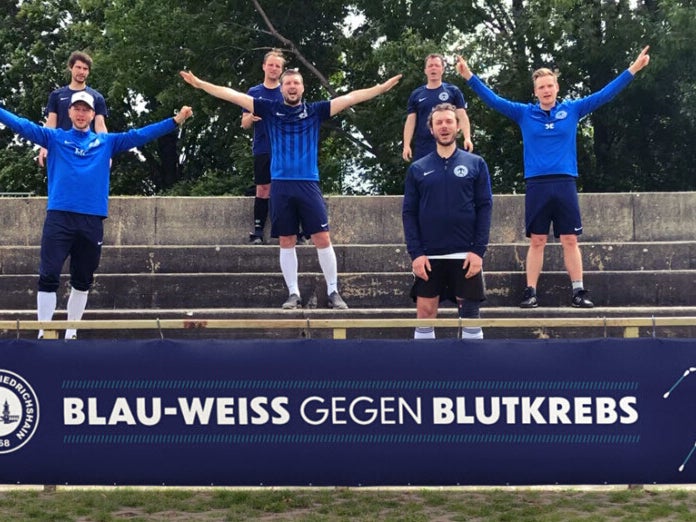 Eine Gruppe von Männern in blauen Uniformen steht mit erhobenen Armen auf einer Treppe. Darunter ist ein Banner mit dem Text "Blau-Weiss Gegen Blutkrebs" Eine Gruppe von Männern in blauen Uniformen steht mit erhobenen Armen auf einer Treppe. Darunter ist ein Banner mit dem Text "Blau-Weiss Gegen Blutkrebs"