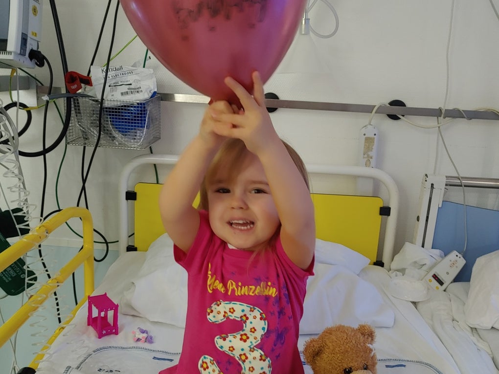 Ein Kind sitzt auf einem Krankenhausbett und hält einen Luftballon Ein Kind sitzt auf einem Krankenhausbett und hält einen Luftballon