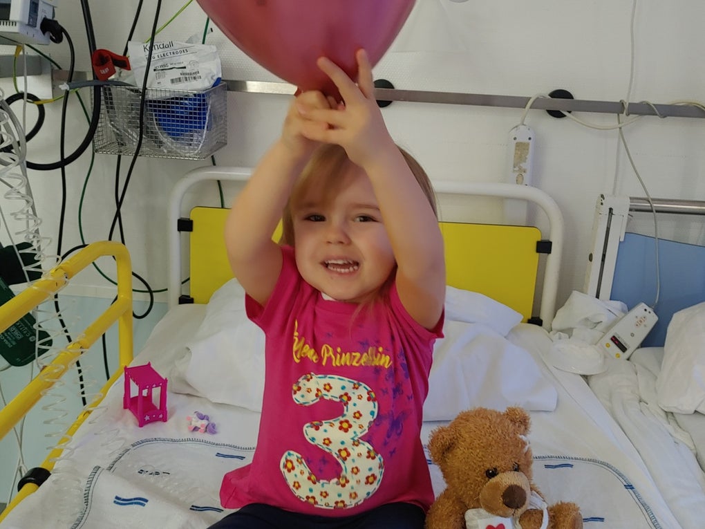 Ein Kind sitzt auf einem Krankenhausbett und hält einen Luftballon Ein Kind sitzt auf einem Krankenhausbett und hält einen Luftballon