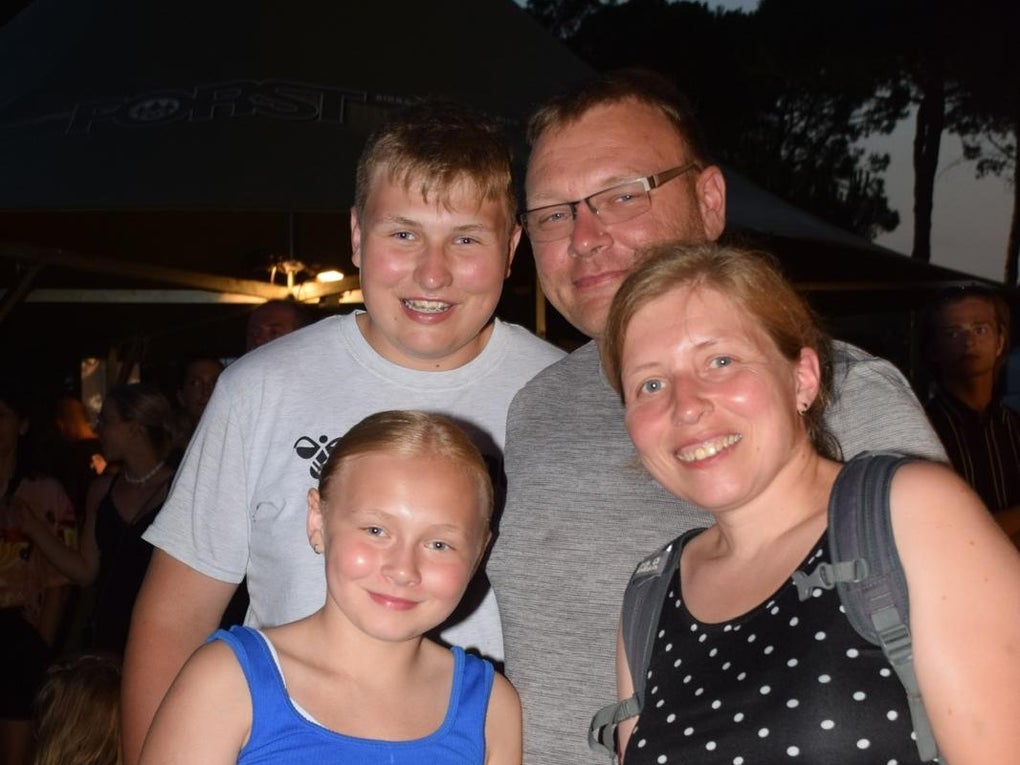 Eine Familie lächelt für ein Foto. Hinten steht ein Junge mit dem Vater, im Vordergrund ein Mädchen und die Mutter Eine Familie lächelt für ein Foto. Hinten steht ein Junge mit dem Vater, im Vordergrund ein Mädchen und die Mutter