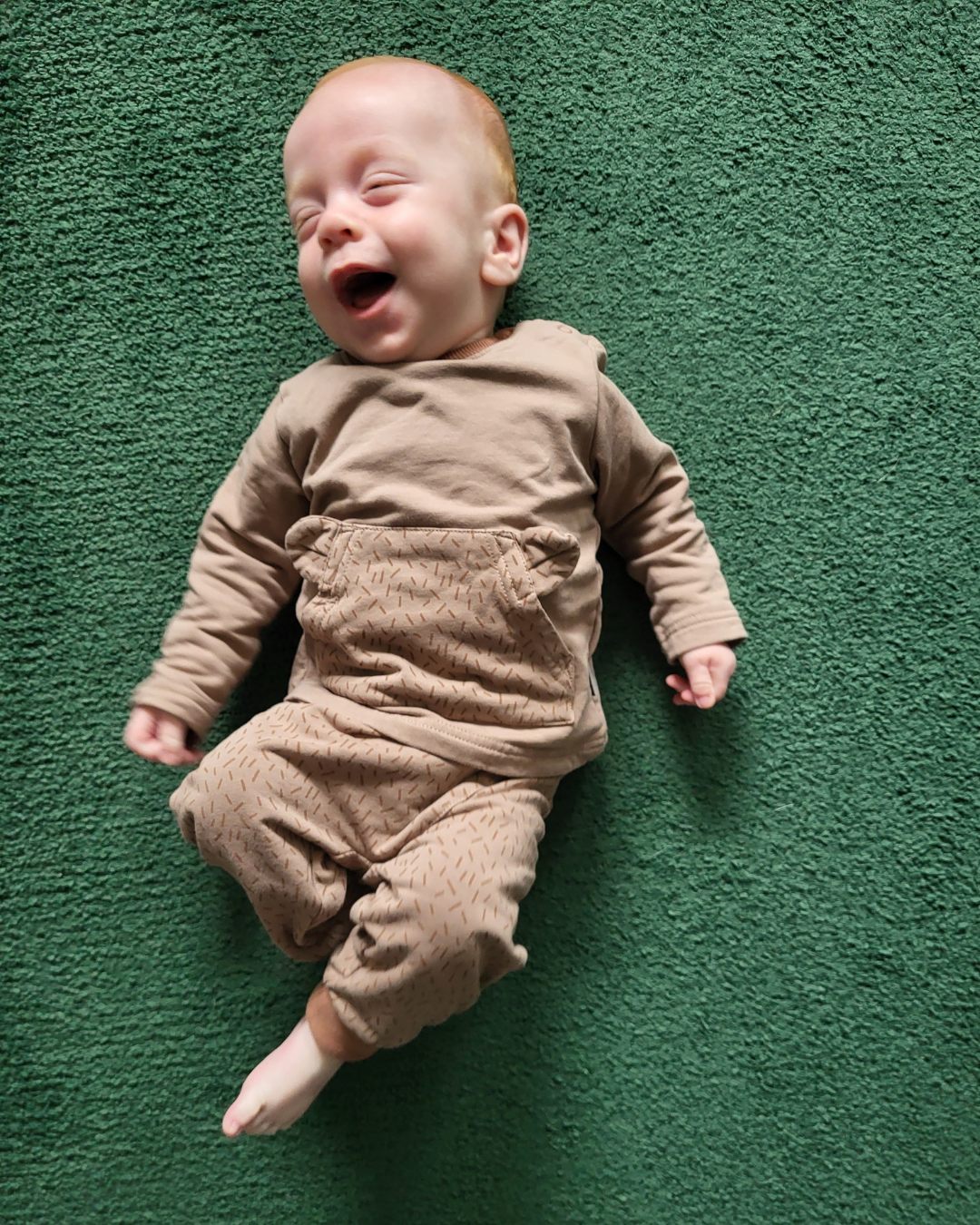 Ein Baby liegt auf einem grünen Teppich Ein Baby liegt auf einem grünen Teppich