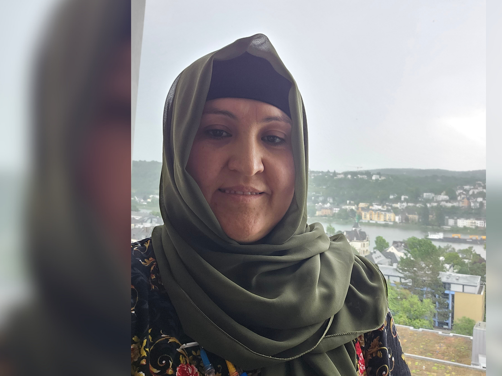 Eine Frau trägt ein olivgrünes Kopftuch und lächelt in die Kamera. Eine Frau trägt ein olivgrünes Kopftuch und lächelt in die Kamera.