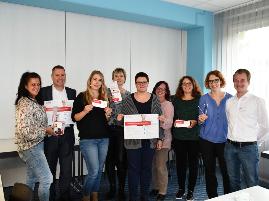 Eine Gruppe von Menschen hält Schilder, Registrierungssets und Wattestäbchen hoch Eine Gruppe von Menschen hält Schilder, Registrierungssets und Wattestäbchen hoch